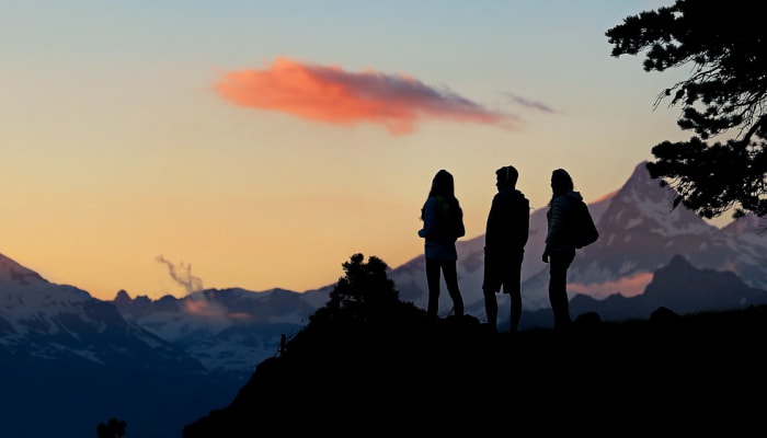 Trois randonneurs en silhouette au coucher de soleil face aux sommets alpins du Grand Paradis