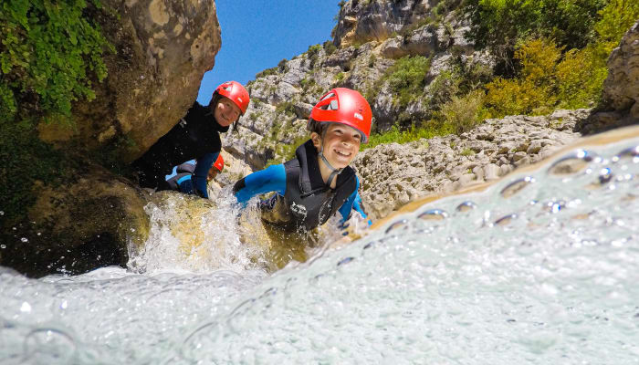 Enfants en canyoning portant casques rouges traversant un ruisseau entre les parois rocheuses du canyon