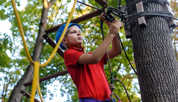 Enfant en équipement de sécurité pratiquant l'escalade en parc aventure multisports