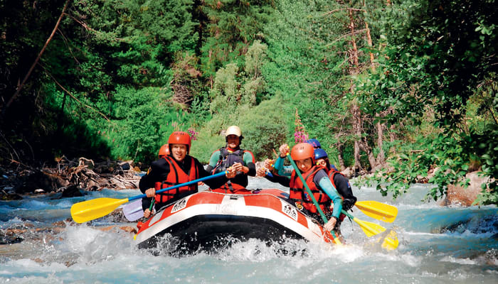 Groupe de participants en rafting équipés de casques et gilets de sauvetage naviguant dans les rapides d'une rivière de montagne