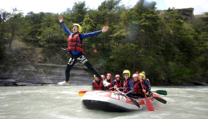 Adolescent en gilet de sauvetage rouge sautant au-dessus d'un radeau avec groupe de jeunes pratiquant le rafting en rivière aux Orres