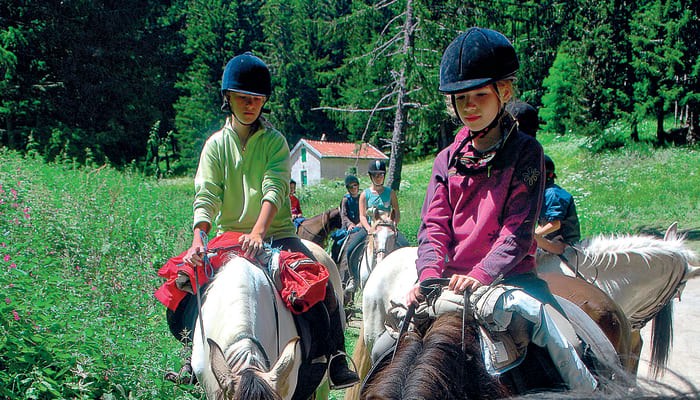 Deux jeunes cavaliers à cheval dans les paysages verdoyants du Vercors lors d'un raid équestre en montagne
