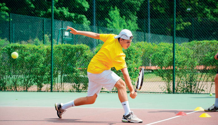 Jeune joueur en tenue jaune exécutant un coup de tennis sur court à Serre Chevalier