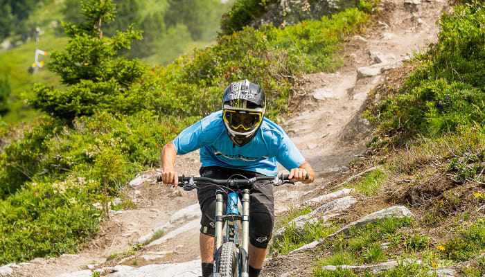 Jeune cycliste en descente VTT sur sentier montagneux aux Arcs avec casque et maillot bleu