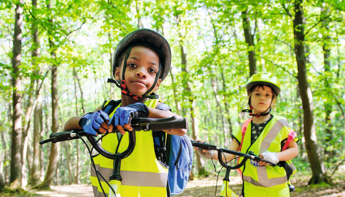 Enfants en gilets de sécurité jaunes pratiquant le VTT sur un sentier forestier avec leurs vélos