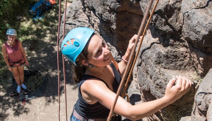 Grimpeur en escalade sur paroi rocheuse avec casque bleu, encordé et assuré par un moniteur UCPA