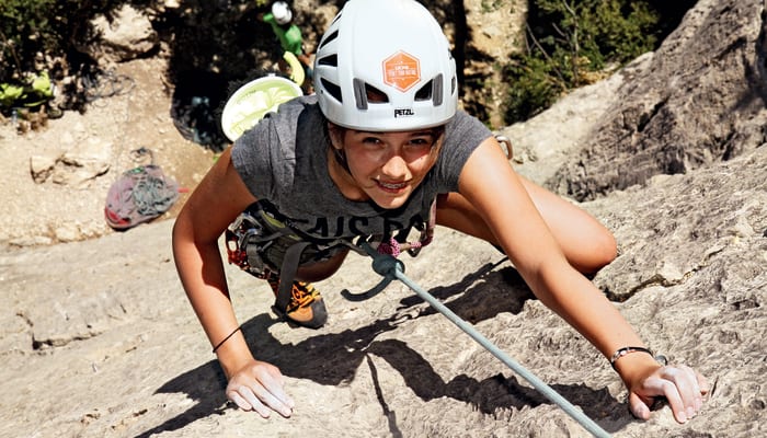 Jeune adolescent en escalade sportive portant casque et baudrier sur paroi rocheuse pour séjour multisports en montagne