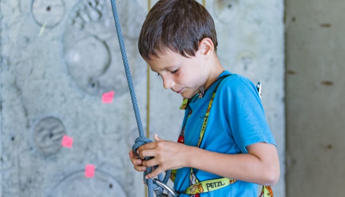 Enfant en escalade intérieure tenant la corde avec harnais et équipement de sécurité sur mur gris