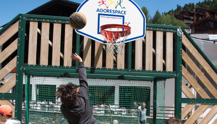Enfant tirant au panier de basket Multi'Ride à la Plagne 1800, structure de jeu en bois et filet vert
