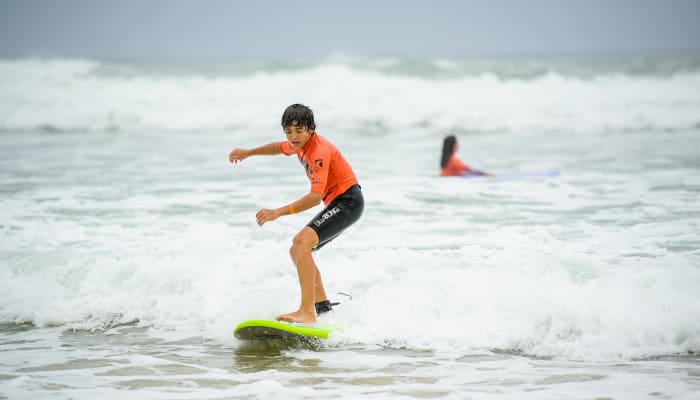Jeune surfeur en équilibre sur sa planche verte dans les vagues avec un moniteur en arrière-plan