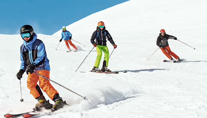 Groupe de skieurs en descente sur piste enneigée avec équipement de ski alpin et casques de protection