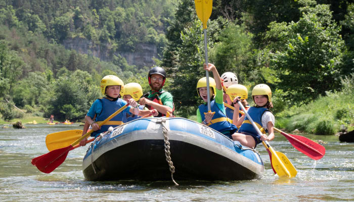Groupe d'adolescents en rafting sur rivière avec gilets de sauvetage et casques, pagaies jaunes, forêt verte en arrière-plan