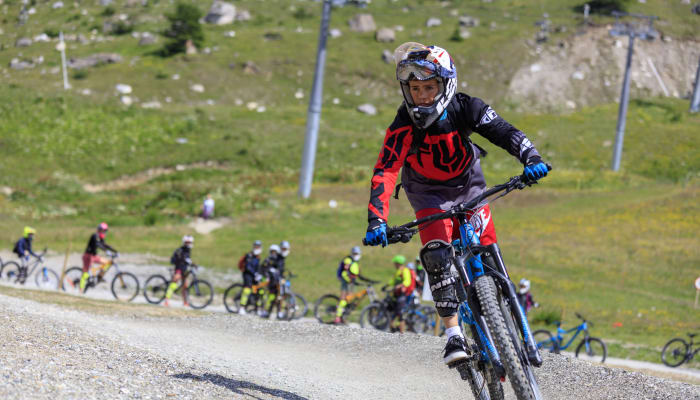 Jeune pilote en VTT de descente sur piste du Bike Park des Arcs avec groupe de riders en arrière-plan