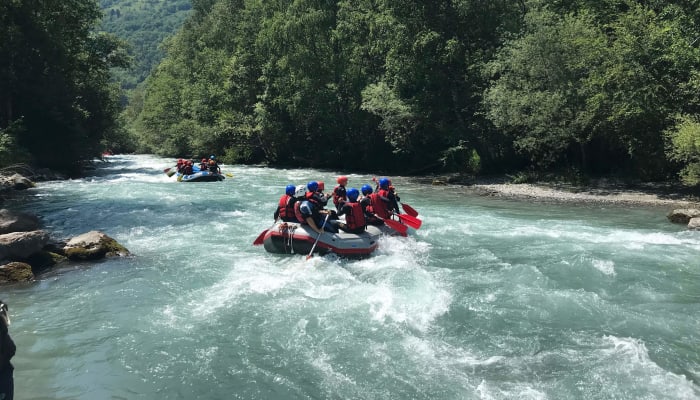 Enfants en rafting sur une rivière turquoise des Pyrénées entourée de forêts verdoyantes lors d'une activité de colo aventure