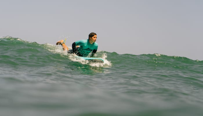 Surfeur en combinaison verte chevauchant une vague verte avec un autre surfeur en arrière-plan