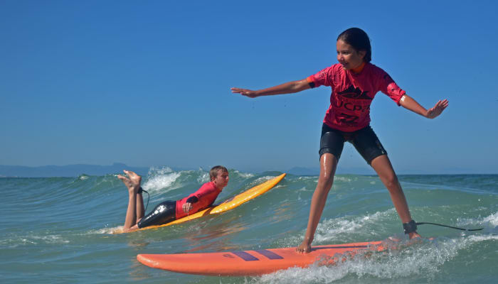 Moniteur de surf en équilibre sur sa planche face à l'océan guidant deux enfants en apprentissage du surf