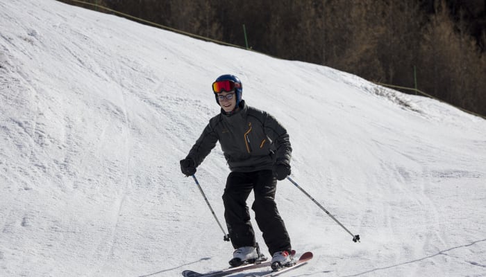 Jeune skieur débutant en tenue noire et casque rouge descendant une piste enneigée à Saint-Lary
