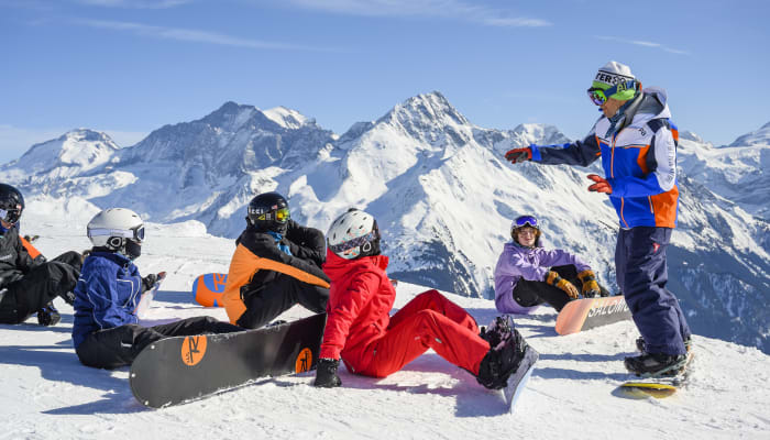 Groupe de jeunes snowboardeurs en pause sur un glacier avec montagnes enneigées aux Arcs