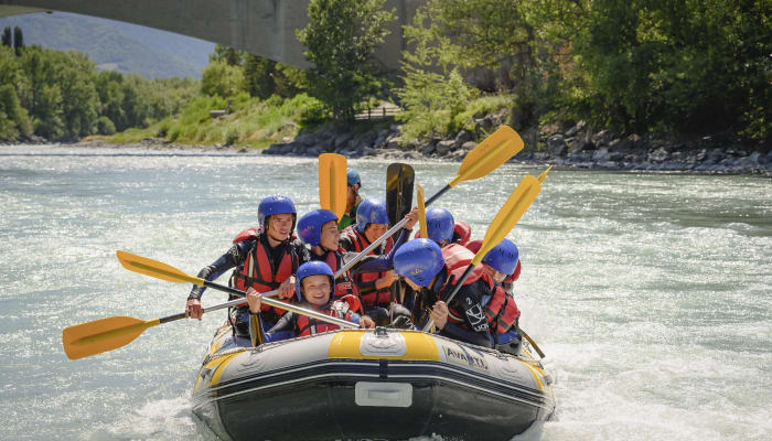 Groupe d'adolescents en rafting sur eaux vives alpines avec pagaies jaunes et gilets de sauvetage bleus