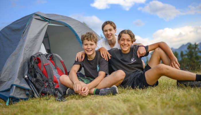 Trois jeunes en séjour multisports en Corse assis devant une tente de camping avec sacs à dos en montagne