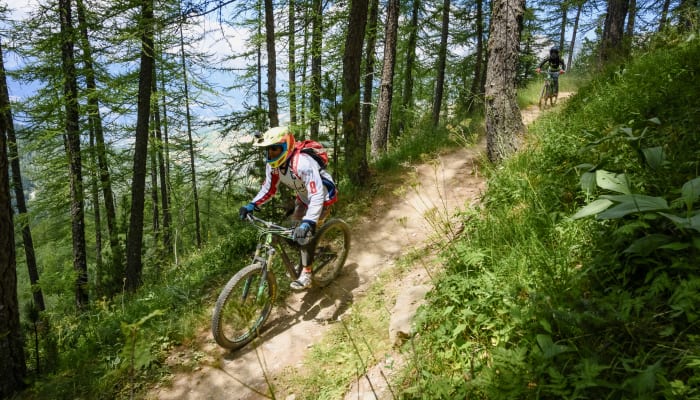 Cycliste en VTT descendant un sentier sinueux en forêt au Bikepark des Arcs, initiation techniques de base