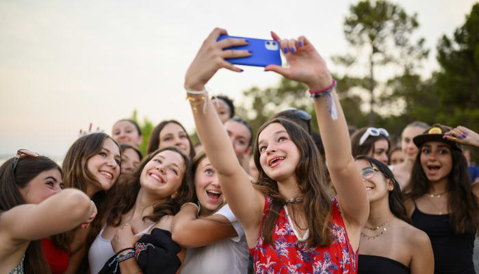 Groupe d'adolescents en Corse prenant un selfie collectif avec un smartphone bleu, sourires joyeux et paysage naturel en arrière-plan