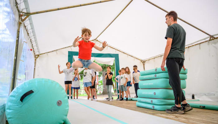 Enfant sautant sur un parcours de multisports en salle avec animateur et groupe d'enfants regardant