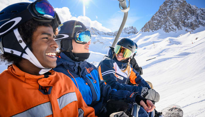 Trois jeunes skieurs et snowboardeurs souriants à Tignes avec des montagnes enneigées en arrière-plan