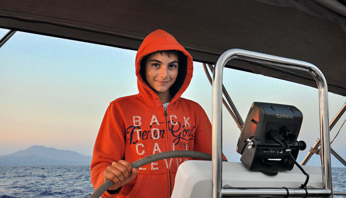 Adolescent en sweat-shirt rouge tenant une pagaie sur un bateau de croisière en Martinique