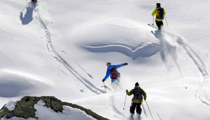 Skieurs en action dévalant des pentes enneigées hors-piste avec crevasses et reliefs montagneux