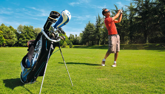 Golfeur en polo rouge exécutant un swing sur un parcours de golf verdoyant avec sac de clubs au premier plan