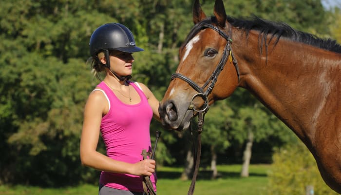 Cavalière en tenue de sécurité avec son cheval bai dans un centre équestre en forêt