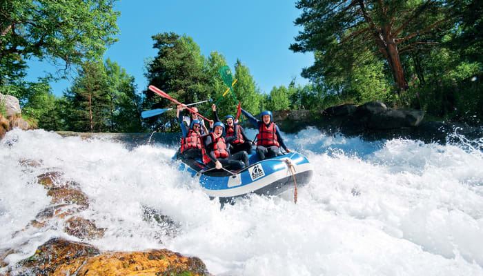 Groupe en rafting sur rapides écumants entouré de forêts des Hautes Alpes, gilets de sauvetage rouge et bleu