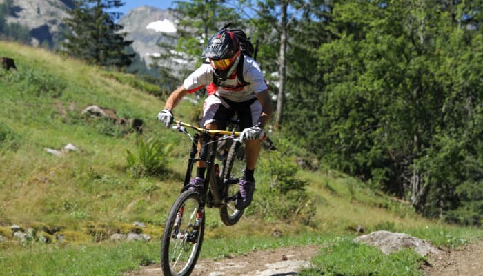 Cycliste en VTT descendant un sentier alpin verdoyant avec casque et équipement de protection près du Mont-Blanc