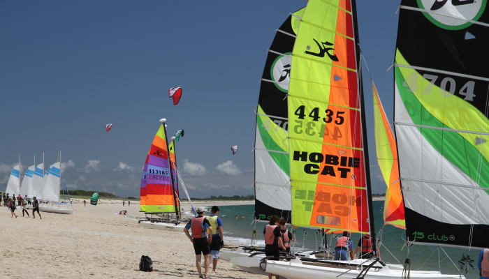 Jeunes participants préparant des catamarans à voile colorés sur la plage de Bénodet pour un stage nautique