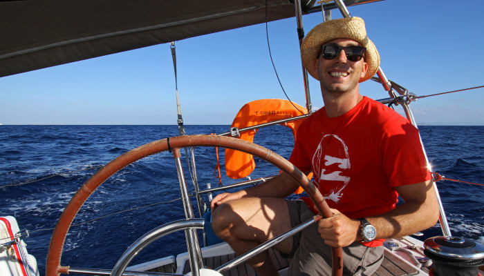 Stagiaire souriant tenant la barre du voilier en Méditerranée lors d'une croisière en Corse