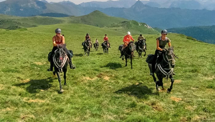 Groupe de cavaliers en randonnée équestre sur les crêtes verdoyantes des Pyrénées avec vue sur le massif de Tabes