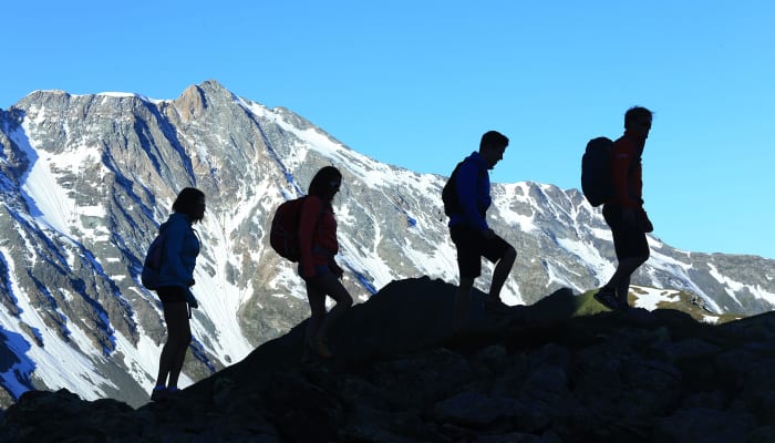 Groupe de randonneurs en trek alpestre dans la vallée de Valgrisenche avec montagnes enneigées en arrière-plan