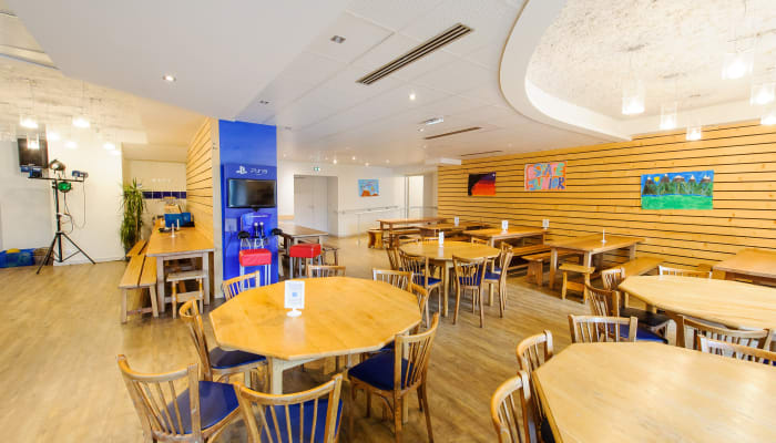 Espace de loisirs moderne à Argentière avec tables rondes en bois, chaises bleues et murs jaunes accueillant familles en vacances