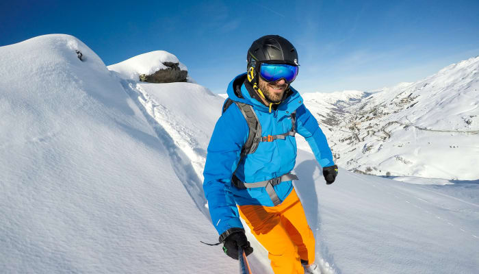 Skieur en veste bleue et pantalon orange descendant une pente enneigée hors-piste en montagne