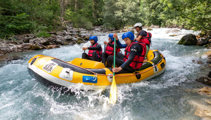 Groupe de jeunes en rafting jaune descendant une rivière tumultueuse en forêt avec gilets de sauvetage bleus