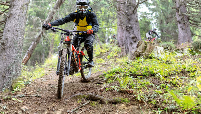 Cycliste en VTT enduro traversant un sentier forestier avec casque et gilet de sécurité jaune dans la vallée du Louron