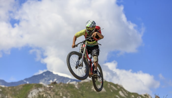 Coureur en VTT descente sautant en l'air sur un terrain montagneux avec paysage alpin en arrière-plan