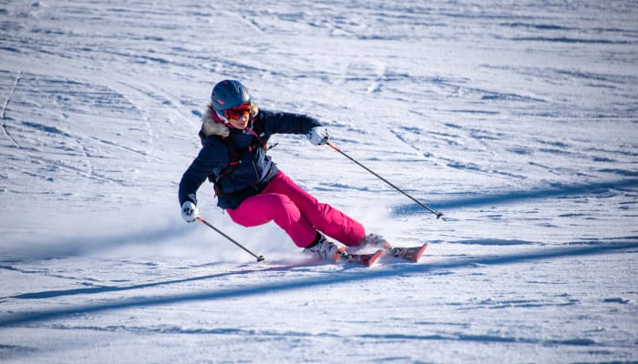 Skieur en action aux Deux-Alpes avec casque bleu et tenue rose descendant une piste enneigée
