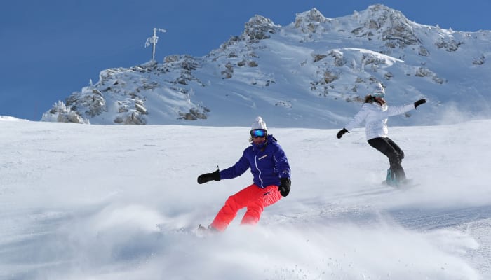 Moniteur et élève en cours de snowboard sur une piste enneigée avec montagne rocheuse en arrière-plan