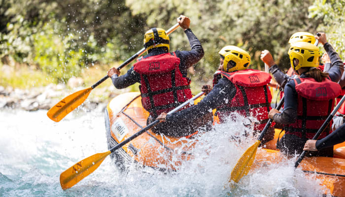 Groupe de pagayeurs en packraft naviguant les rapides de l'Isère avec casques jaunes et gilets de sauvetage rouges
