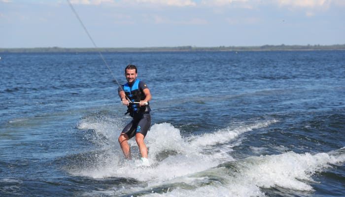 Pratiquant de wakeboard en action sur le lac de Carcans, tracté par un câble, gilet de sauvetage bleu, conditions calmes et ensoleillées