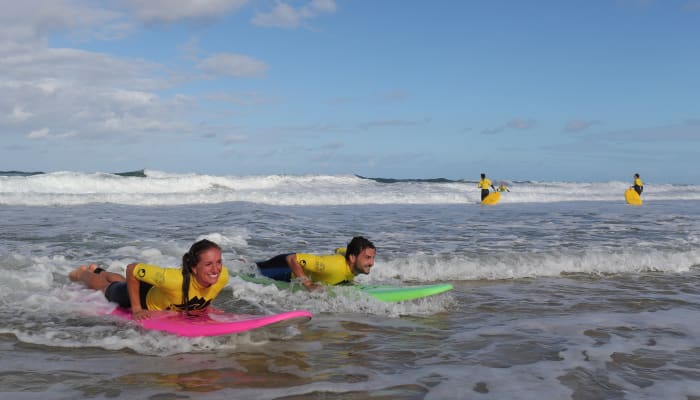 Moniteurs en gilets de sauvetage jaunes initiant des enfants au surf sur planches colorées dans l'océan avec vagues