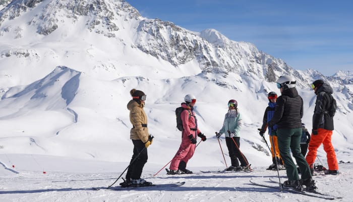 Groupe de skieurs et snowboardeurs sur piste enneigée face à massif montagneux enneigé en Vallée de la Guisane