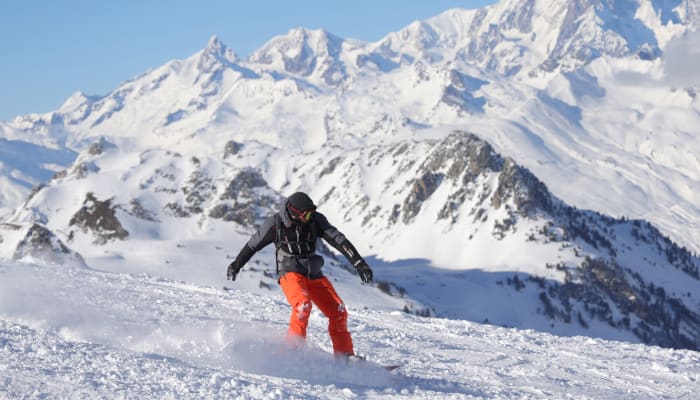 Skieur descendant une piste enneigée avec vue sur des sommets alpins enneigés et ciel bleu dégagé